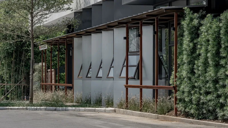 Side facade: timber screen with awning windows propped open, original concrete building visible above, bamboo planting