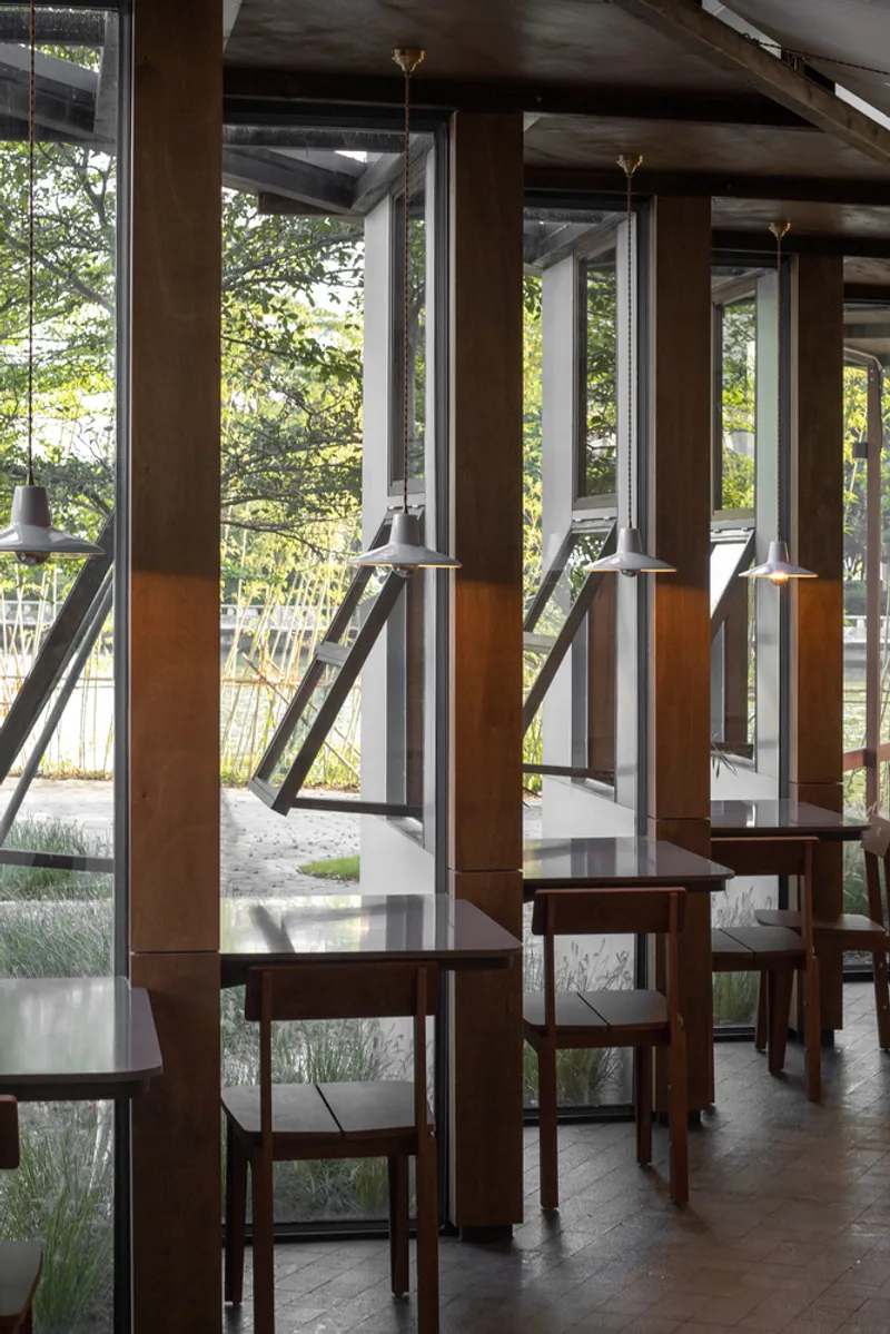 Window counter: timber-framed glass with awning windows tilted out, bar stools, view to greenery beyond