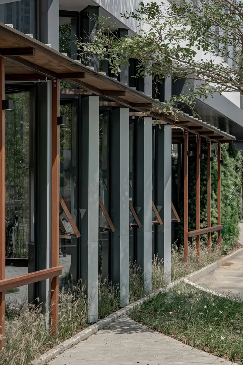 Exterior: timber columns and beams added to the existing concrete building, awning windows, weeds growing along the path