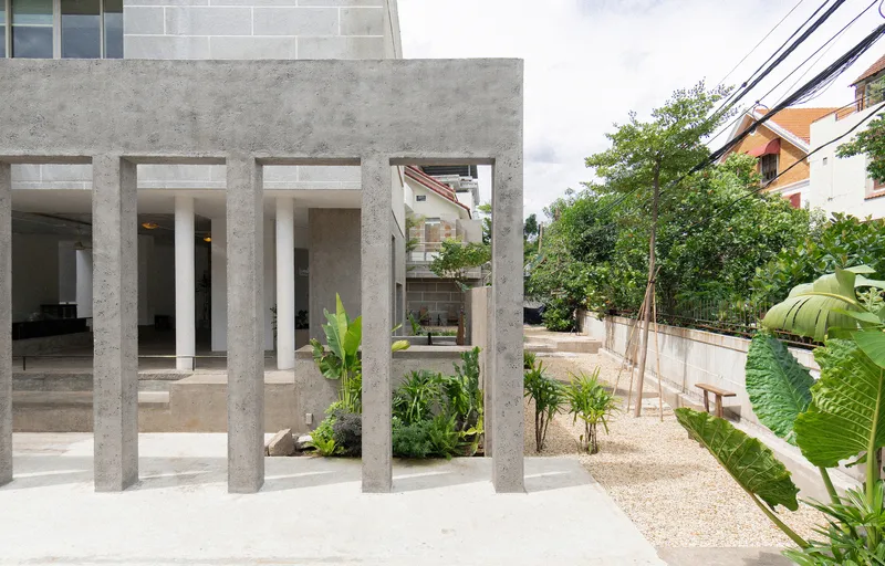 Concrete colonnade framing glass openings and a planted courtyard with gravel and young trees