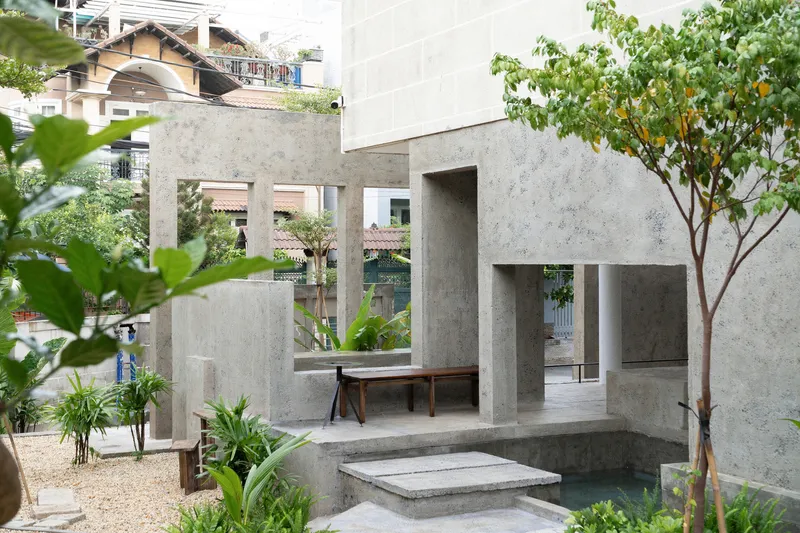 Concrete pavilion with slender columns and benches in a gravel courtyard planted with tropical trees