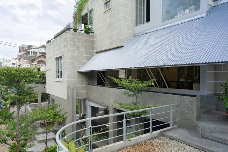 Concrete block facade with corrugated metal canopy and curved steel railing beside planted terrace