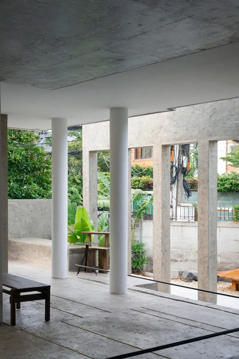 Interior space with round white columns and exposed concrete ceiling opening to garden beyond