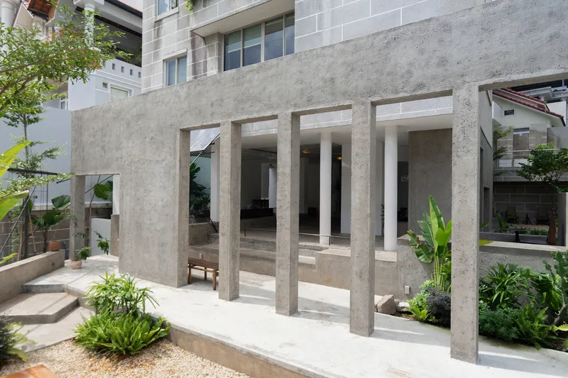 Courtyard view showing concrete colonnade with tall rectangular piers surrounding planted beds and gravel