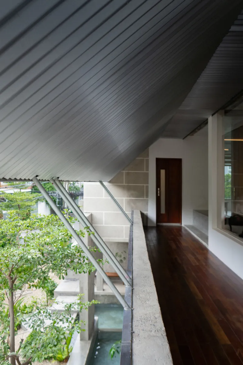 Terrazzo staircase rising beneath a corrugated metal soffit with glass railing overlooking interior pool and foliage