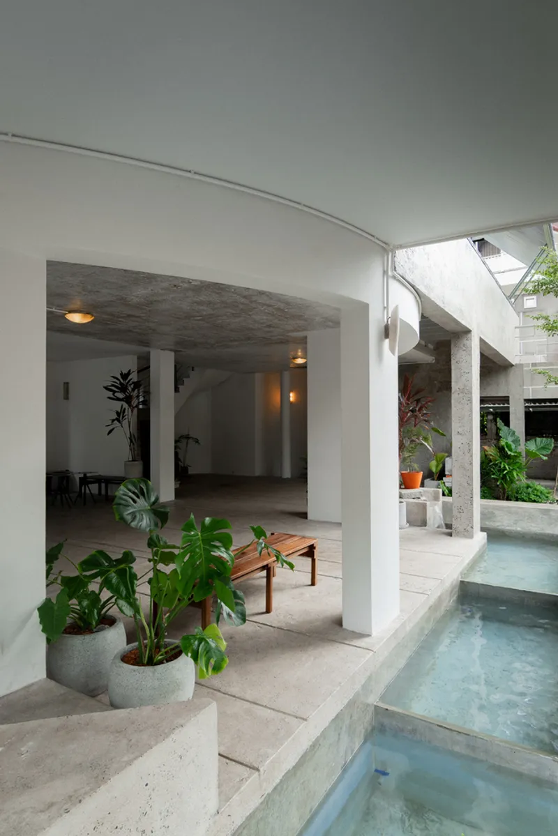 Curved ceiling over a white column and timber bench beside a stepped concrete pool with plants
