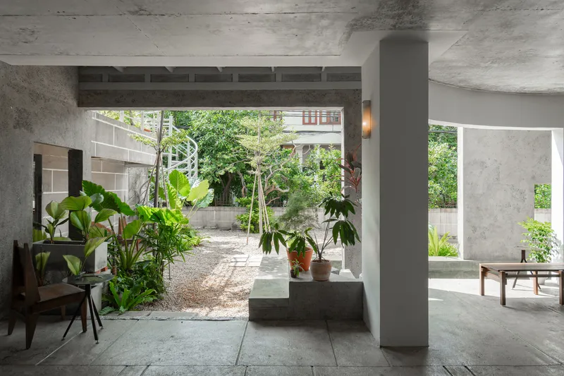 Open-plan interior with concrete columns and ceiling framing a view to the planted gravel courtyard