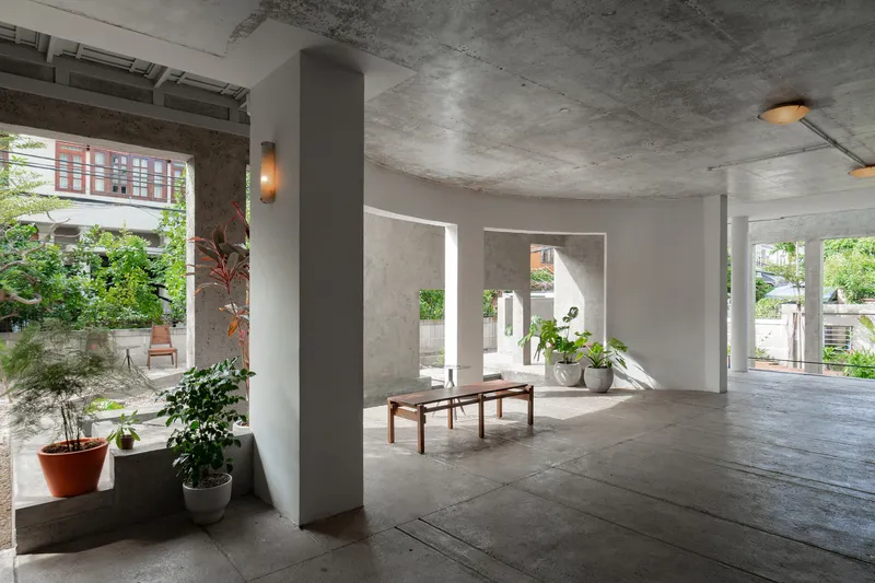 Concrete floor and ceiling with cylindrical columns framing views to garden and adjacent rooms