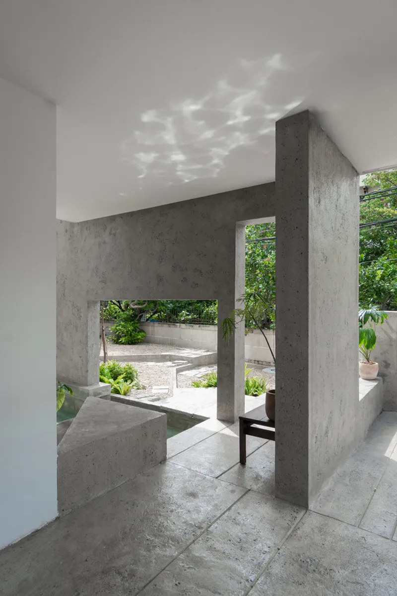 Concrete portal frames with horizontal openings filtering dappled sunlight from the courtyard