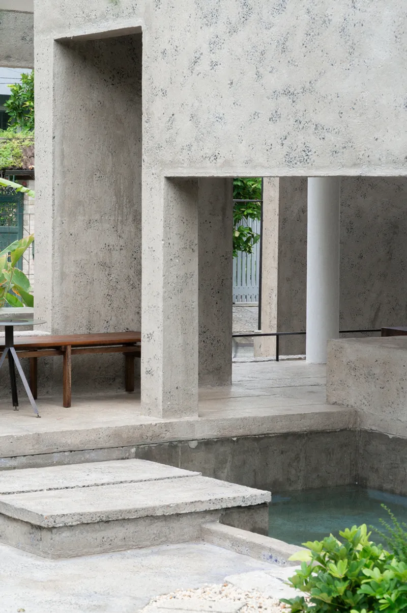 Concrete pavilion with stepped platform and shallow water pool beside a timber bench