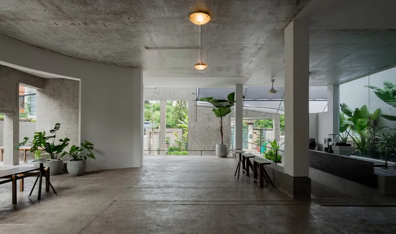 Concrete interior with exposed ceiling, pendant lights, and potted plants beside wooden benches