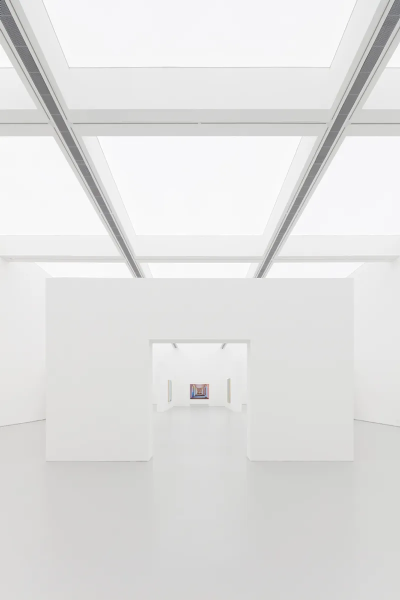 Enfilade: deep perspective through aligned white openings, luminous ceiling panels above, a single small painting at the far end