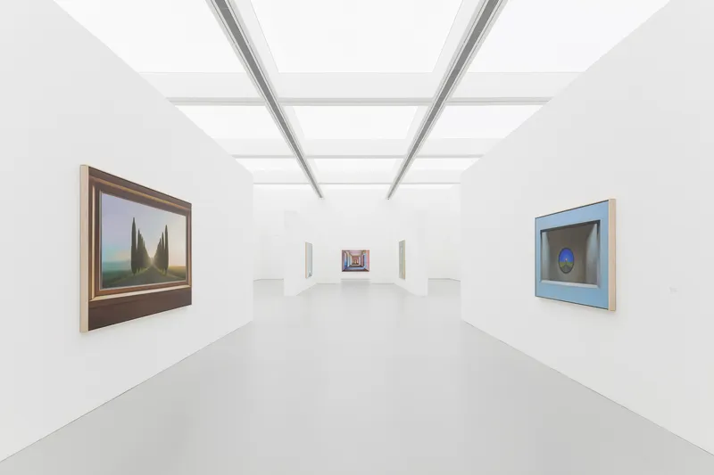First-floor gallery: white walls, grey polished floor, linear skylight ceiling, paintings hung on freestanding partition walls