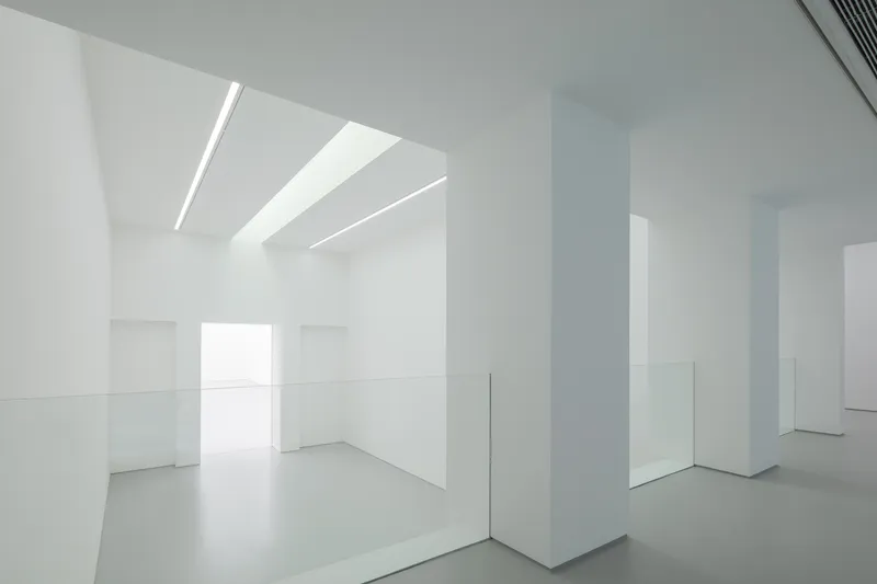 Upper level interior: white columns, glass balustrade, linear ceiling light, volume open to the floor below, window at the far end