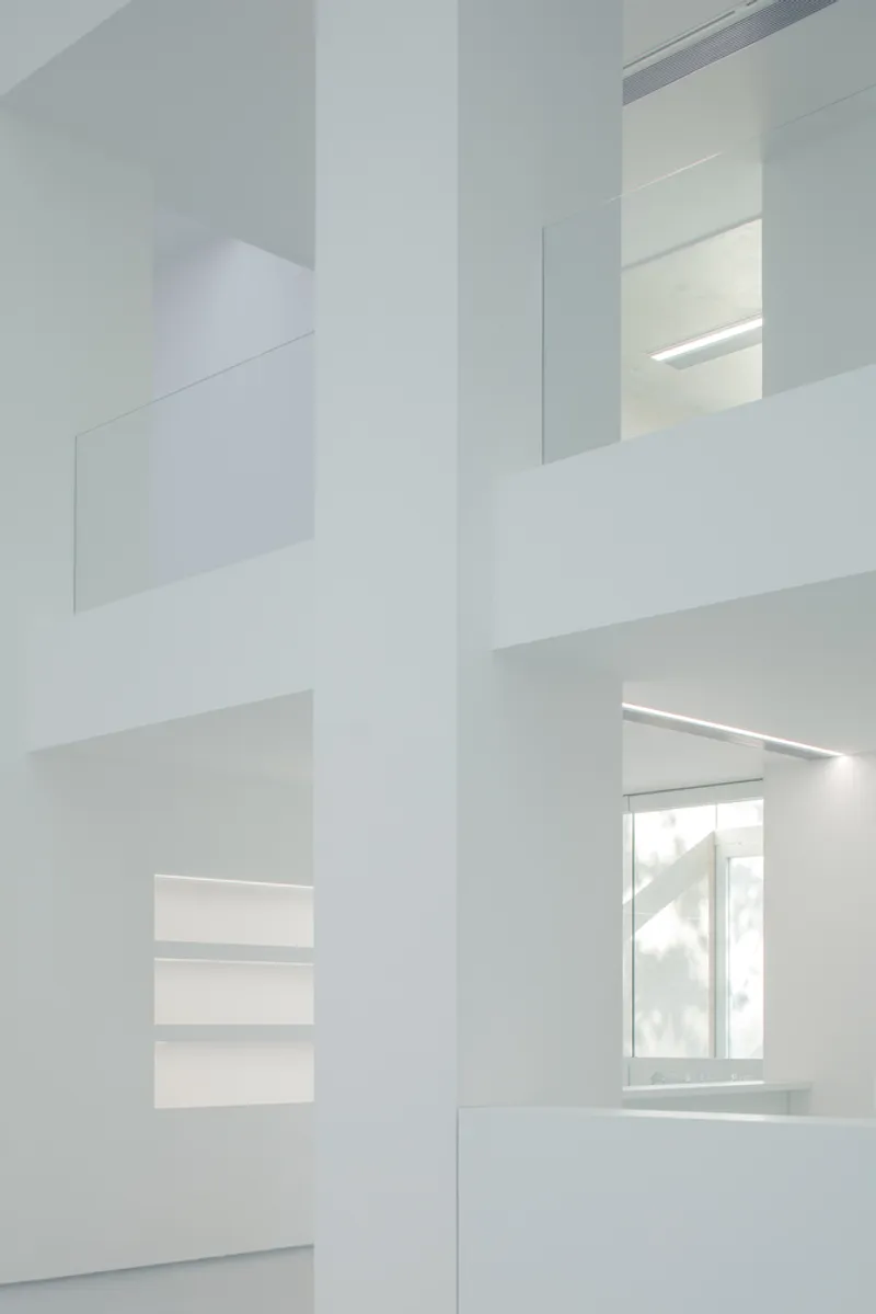 Atrium detail: white walls at multiple levels, glass balustrades, linear lights, window visible through layered openings