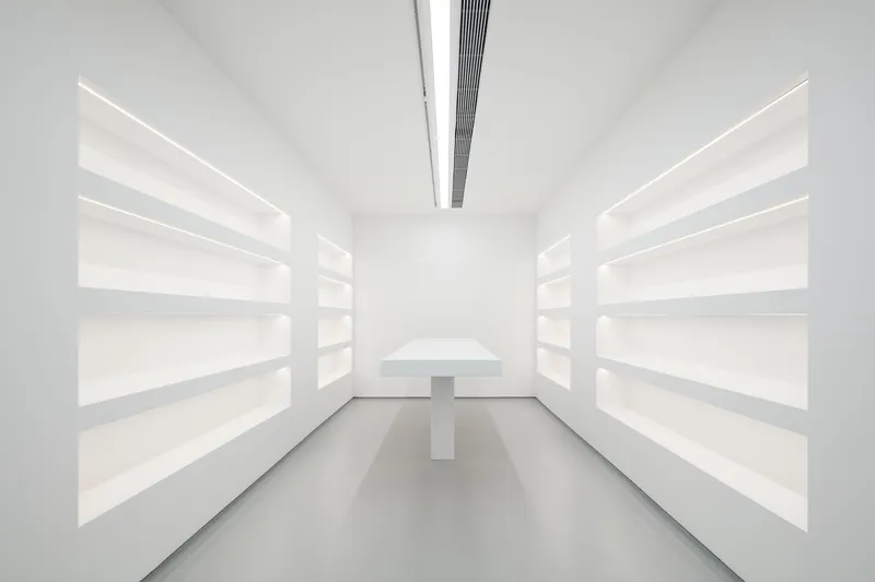 Archive or shop: white shelving on both walls, central display table, linear ceiling light, grey floor