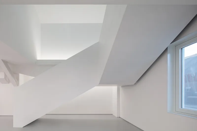 Stair underside: angular white planes meeting at the ceiling, skylight strip, window to the street visible at right