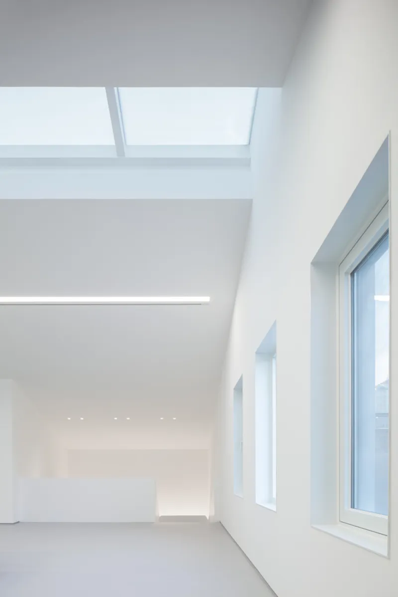Second-floor gallery: skylight above, double-height window wall to the street, white walls, recessed ceiling lights below