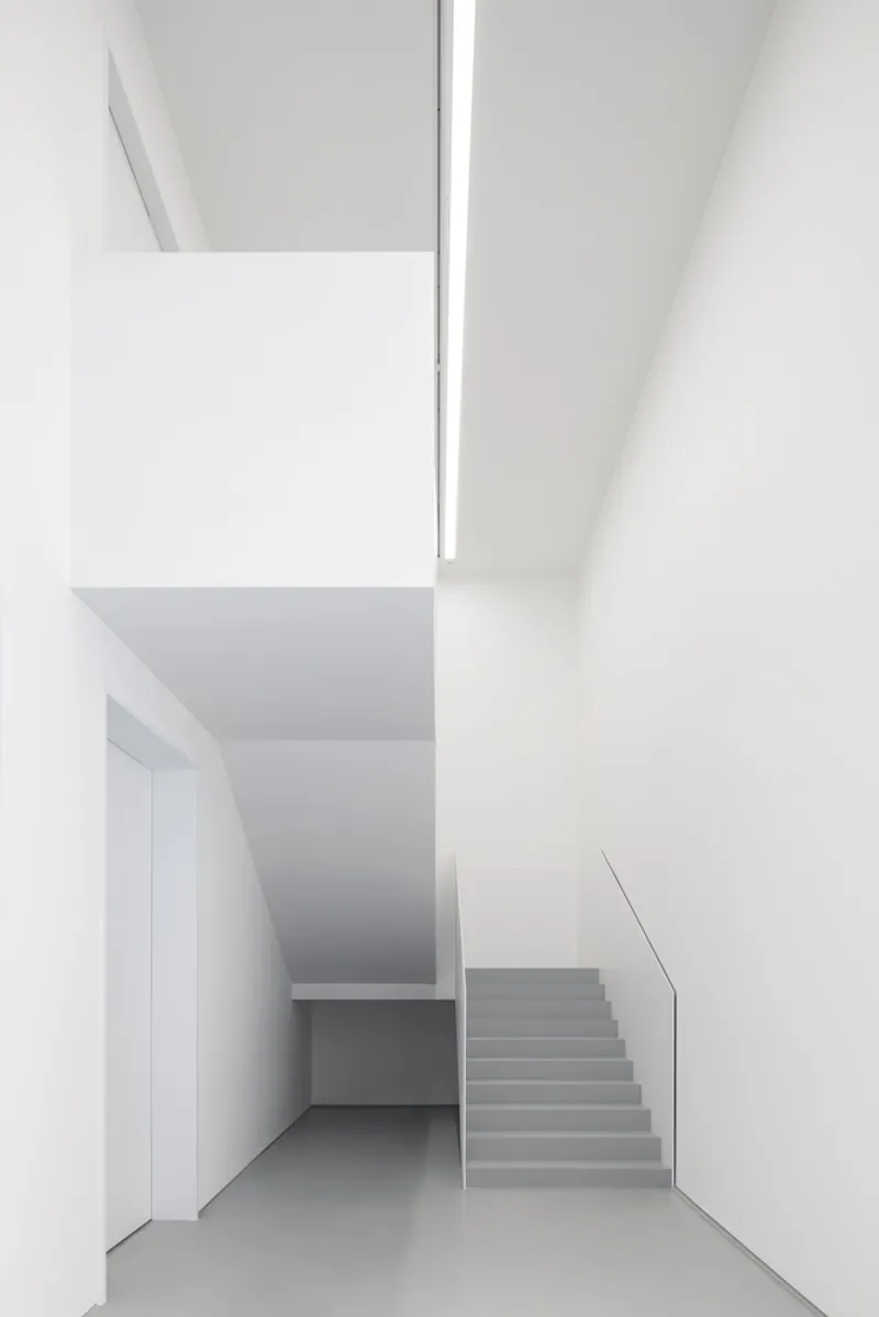 Stairwell: white walls, grey stairs with glass balustrade, double-height void, linear skylight above