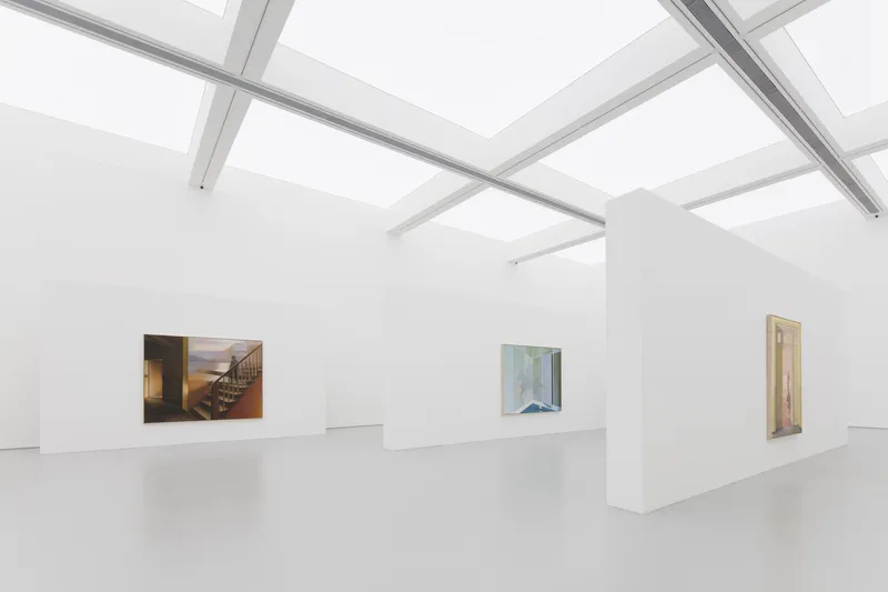 Facade detail: three tall glass openings between white concrete columns, wavy logo above, tree shadows, morning light