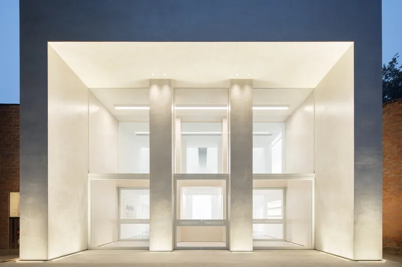 Gallery wall: large painting on a white partition, skylight ceiling with steel beams, second painting visible beyond
