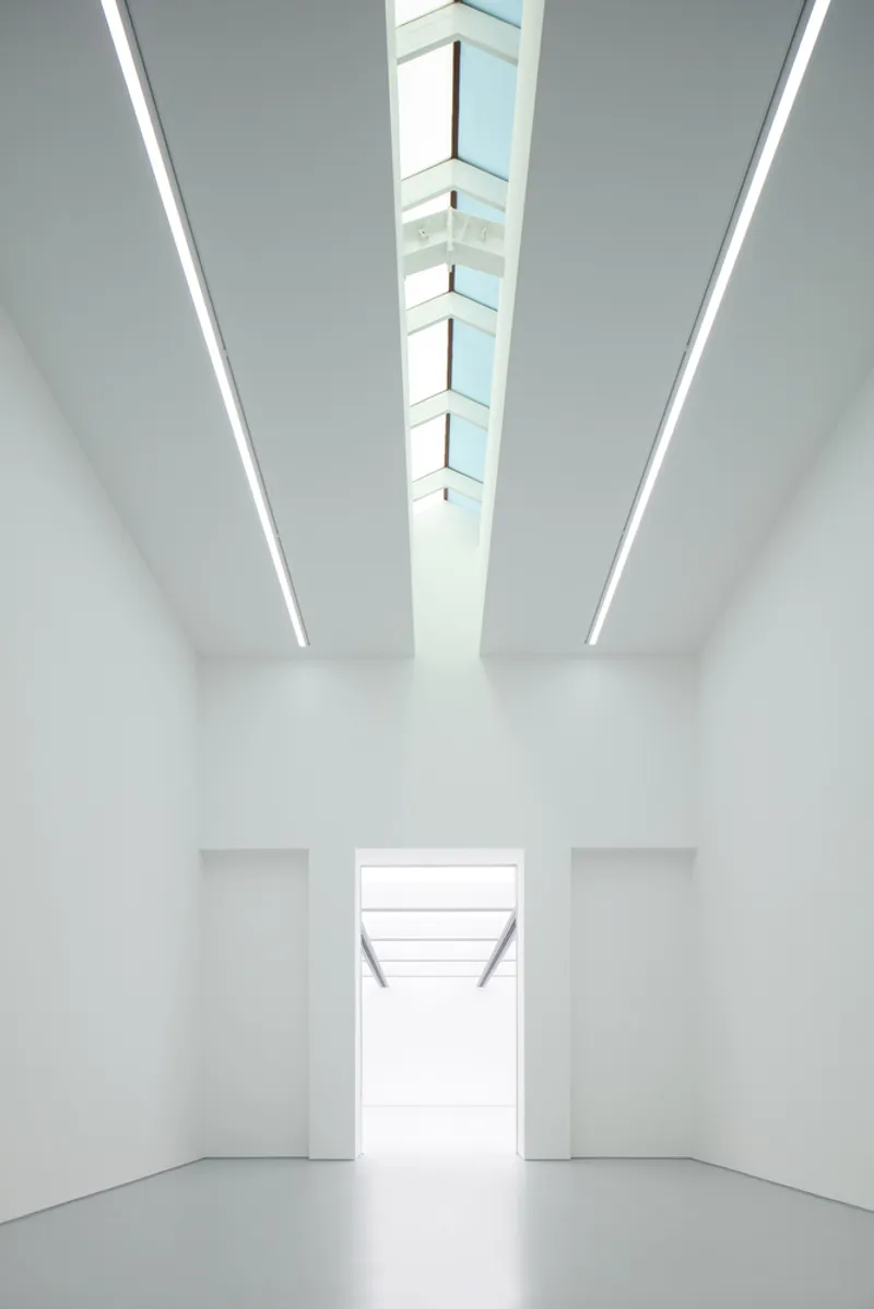 Lobby perspective: skylight strip above, white walls converging toward a bright opening, grey polished floor