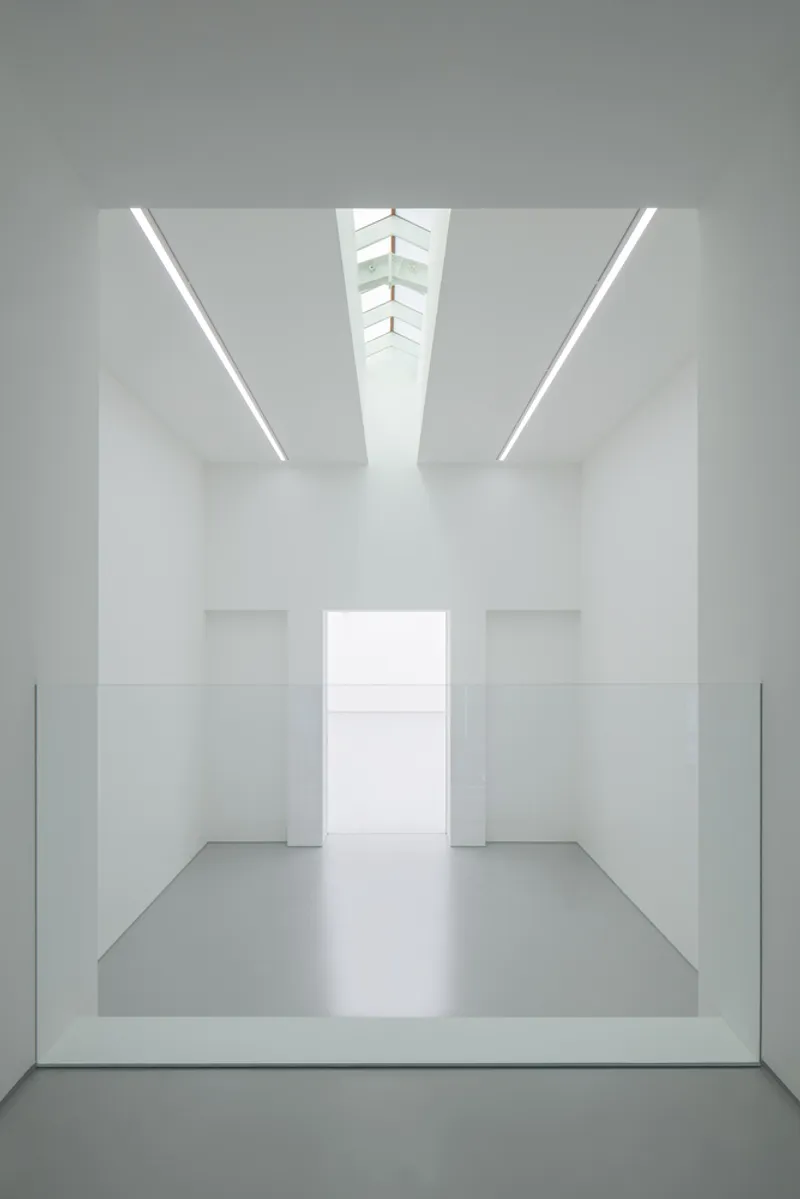 Second-floor void from above: glass balustrade at the edge, white walls, skylight converging above, gallery below