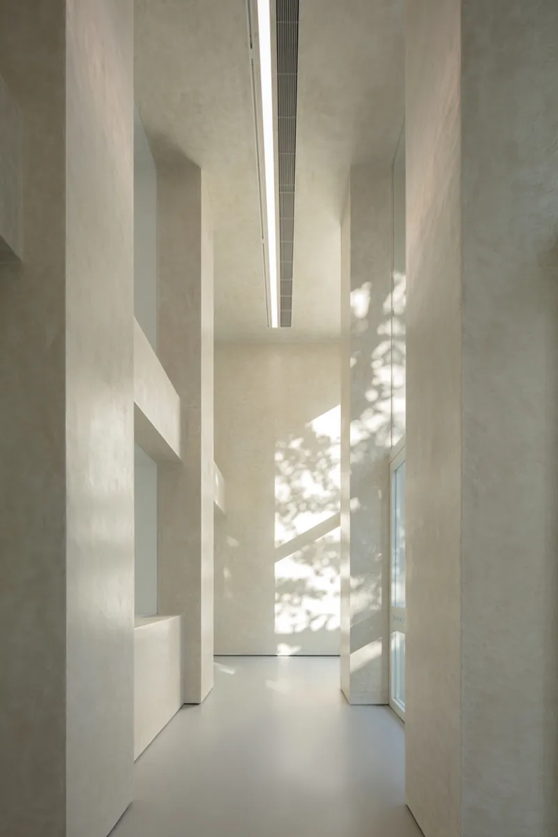 Facade at night: warm light flooding through the three glass openings, white concrete glowing, columns casting shadows