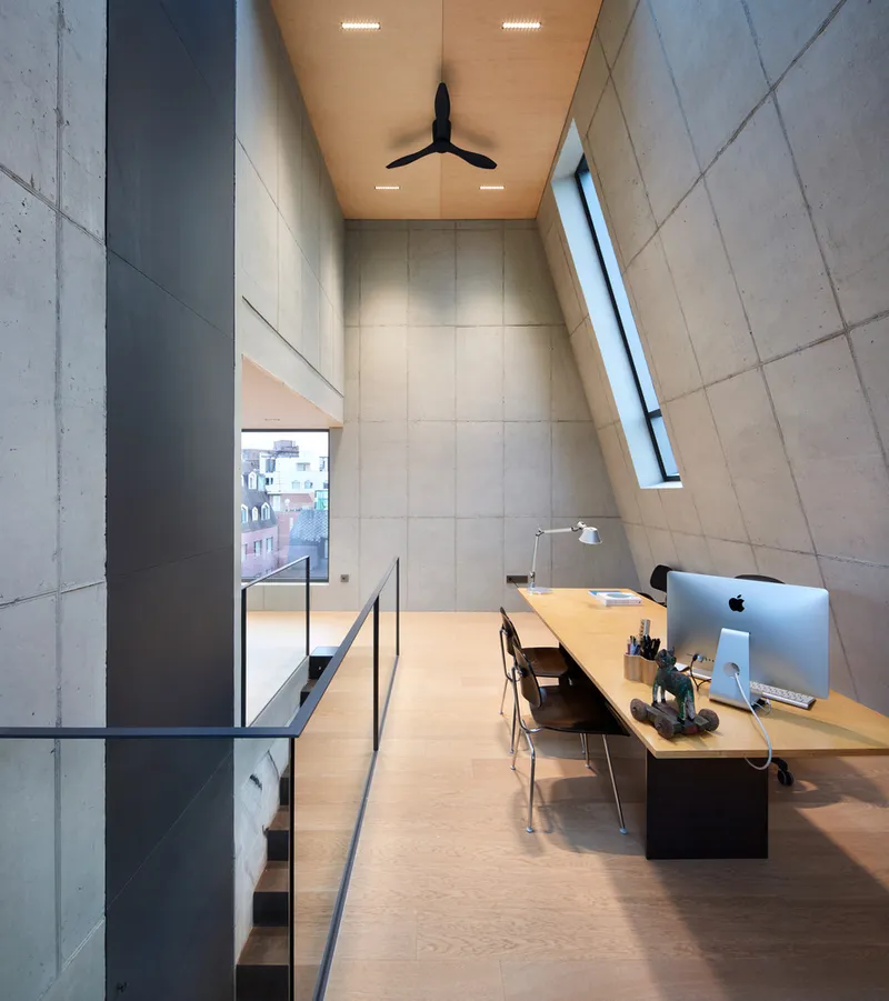 Dusk rooftop view: the angular dark-brick top with illuminated interior, terracotta roofs around, overcast sky