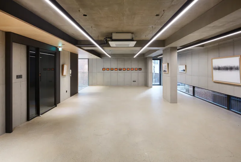 Living room: double-height concrete space with angular ceiling, sofa, round table, full-height window to the street