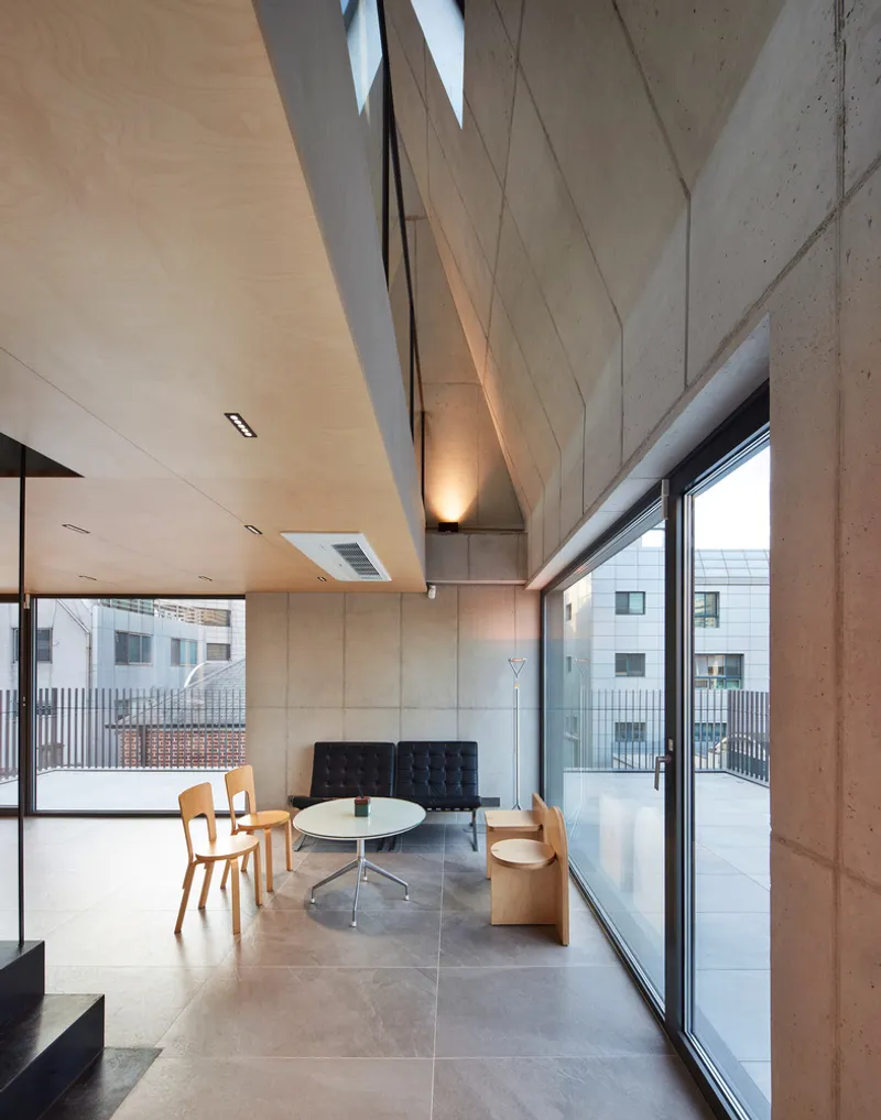 Top floor study detail: timber desk along concrete wall, birch ceiling panel, angular skylight above, glass railing