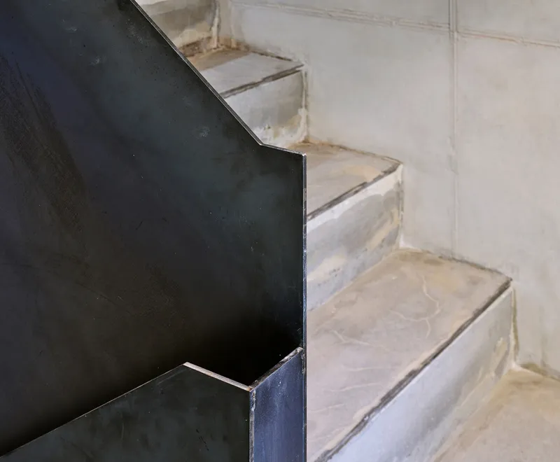 Stair void: looking down through a narrow concrete shaft with spiral stair, skylight above, birch ceiling visible