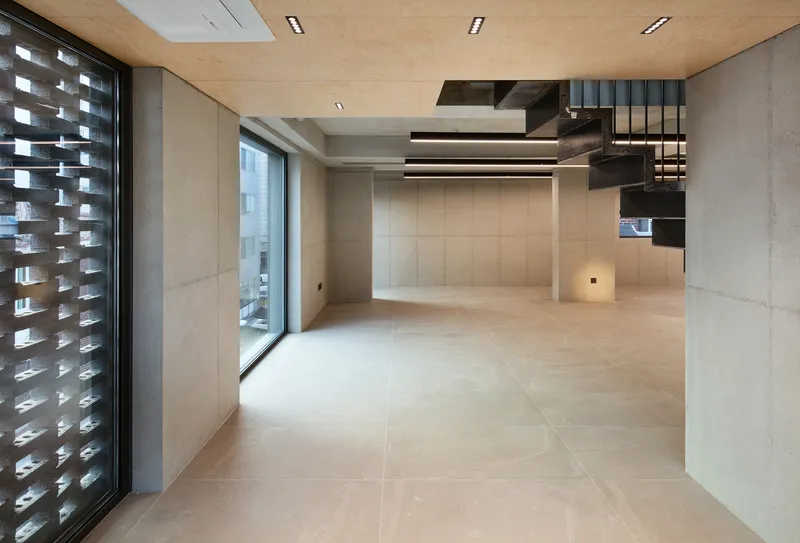 Mezzanine void: dark steel column, glass railing, birch ceiling above, concrete walls, street view through window