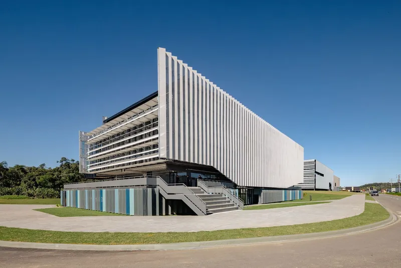 Corner view of the vertical white louvred facade above a lower level with striped panels and entry stairs