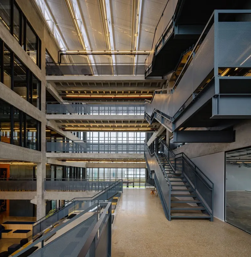Multi-storey atrium with exposed concrete slabs, metal staircases, and skylights filtering daylight from above