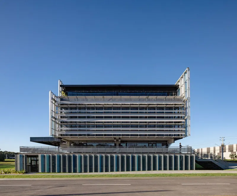 Cantilevered concrete structure with horizontal sun shading and vertical striped base under clear blue sky