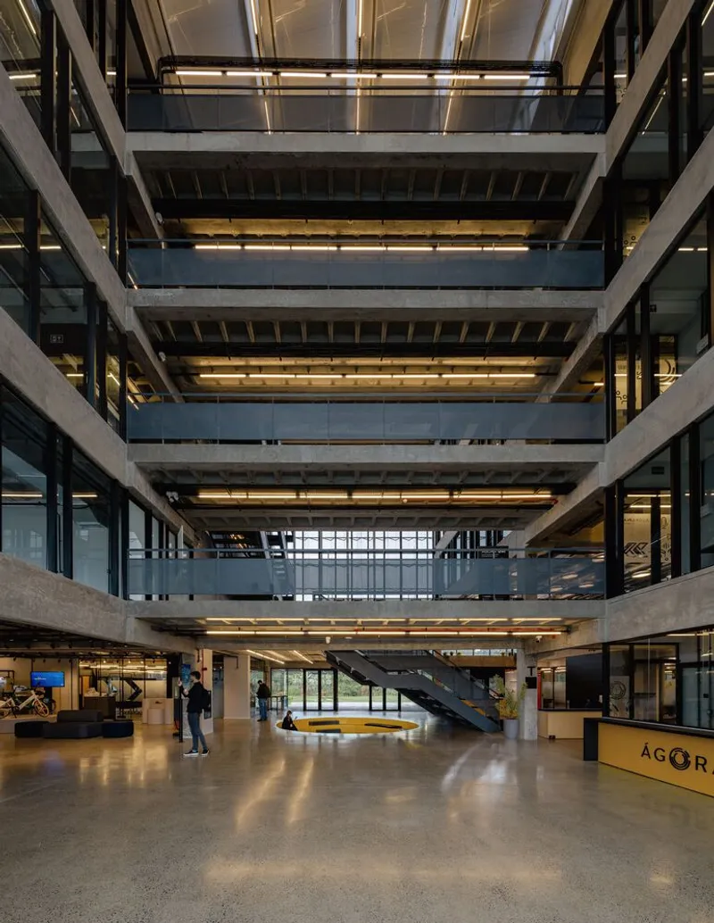 Central atrium with exposed concrete slabs, steel staircases and people crossing the polished floor at dusk