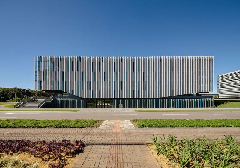Frontal view of the vertical white louvre facade across a paved walkway with planted beds
