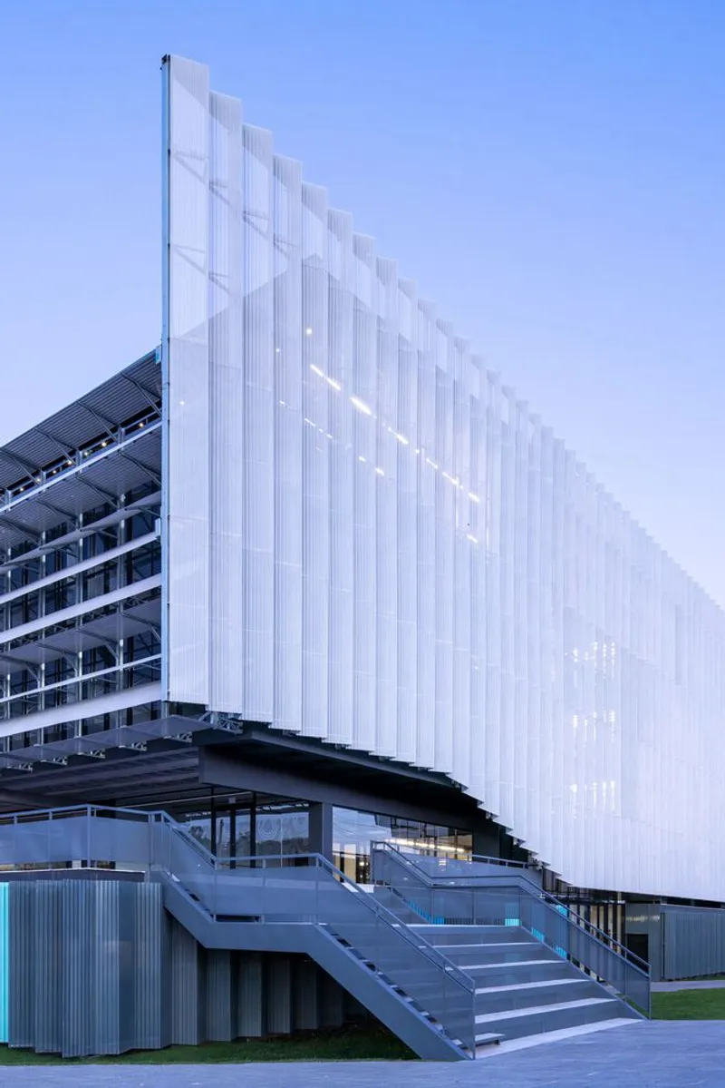 Exterior stair leading to the elevated entrance beneath the translucent vertical screen facade at dusk