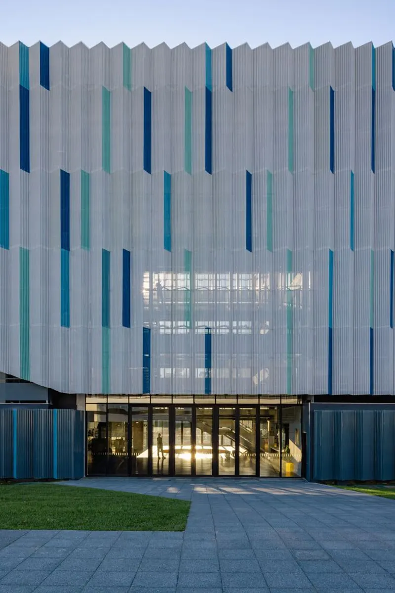 Ground-level entrance with glass doors below the white and blue vertical fin facade at twilight