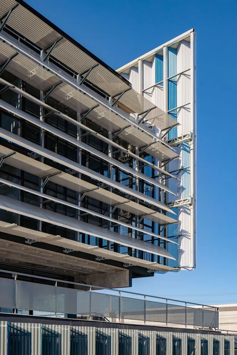 Angled view showing the exposed concrete floor slabs and the vertical louvered screen against blue sky