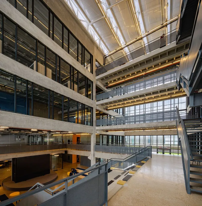 Multi-story atrium with exposed concrete beams, glazed partitions, and open staircases under a translucent roof