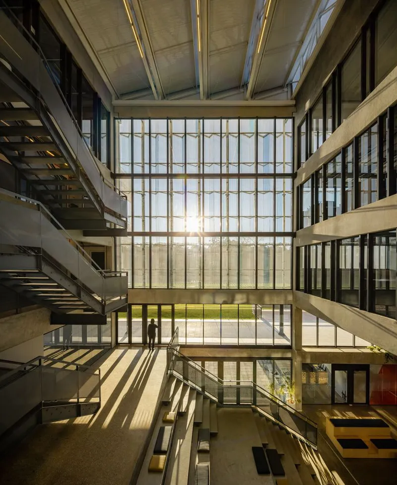 Interior atrium view with sunlight streaming through the gridded glazing and casting shadows on concrete floors