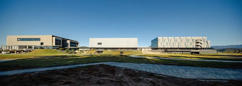Campus view showing three separated volumes across a grassy landscape with a reflecting pool in the foreground