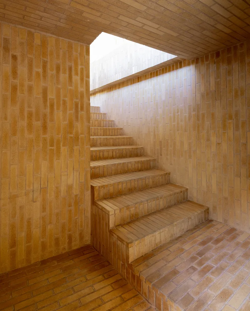 Brick staircase: a rising run of stairs clad in the same warm geometric brick as the walls, with deep shadow and soft top-lit daylight