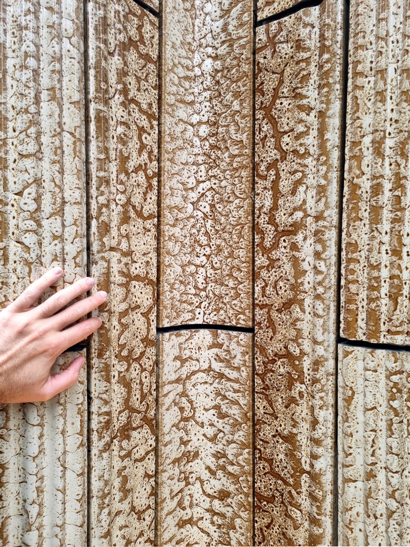 Close-up of textured hempcrete wall panels with a hand touching the surface in natural light
