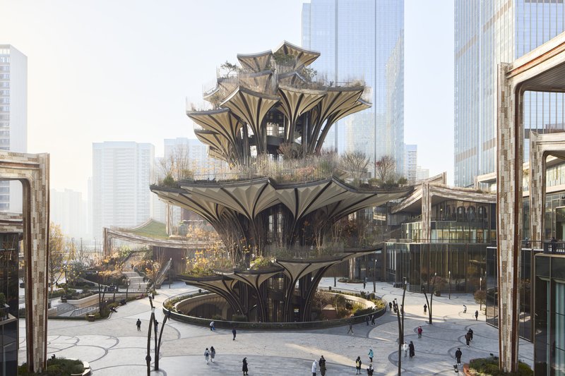 Tiered structure with arching bronze columns and planted terraces rising above a public plaza with pedestrians