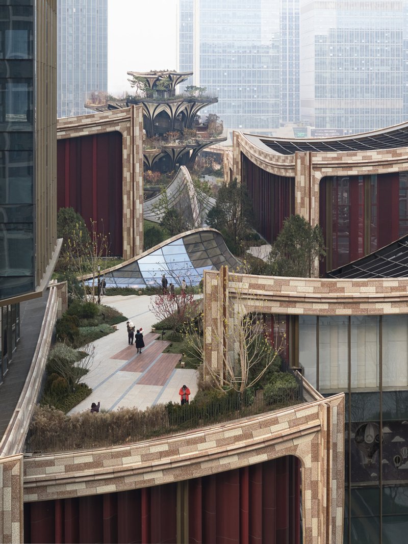 Rooftop gardens with curved planted beds and paved pathways winding between buildings in hazy daylight