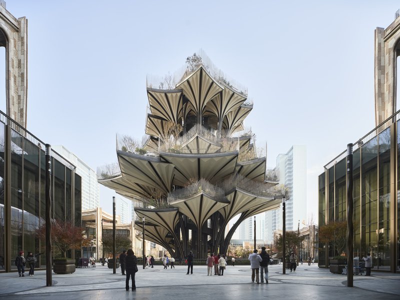 Central tower structure with stacked fan-shaped canopies and rooftop planting viewed from public plaza