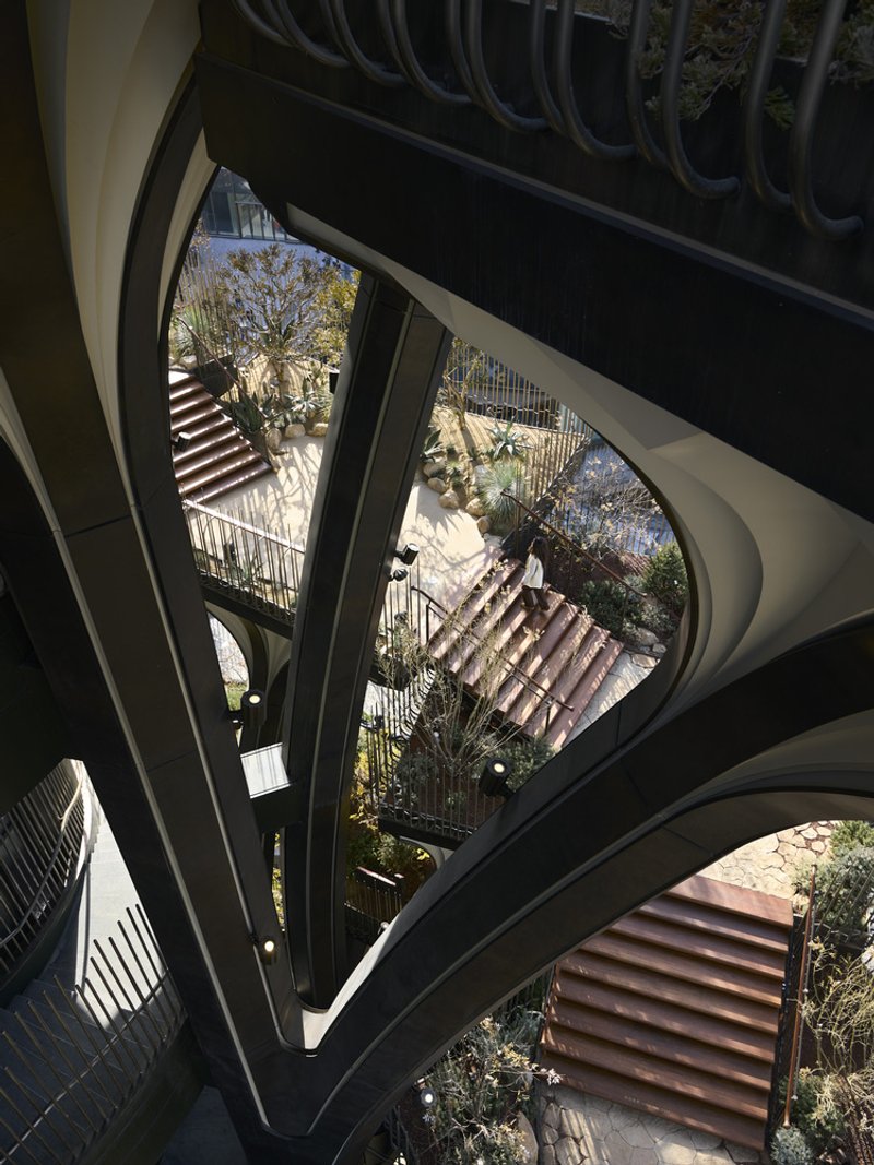 View down through the triangular atrium void showing planted terraces and staircases in dappled sunlight